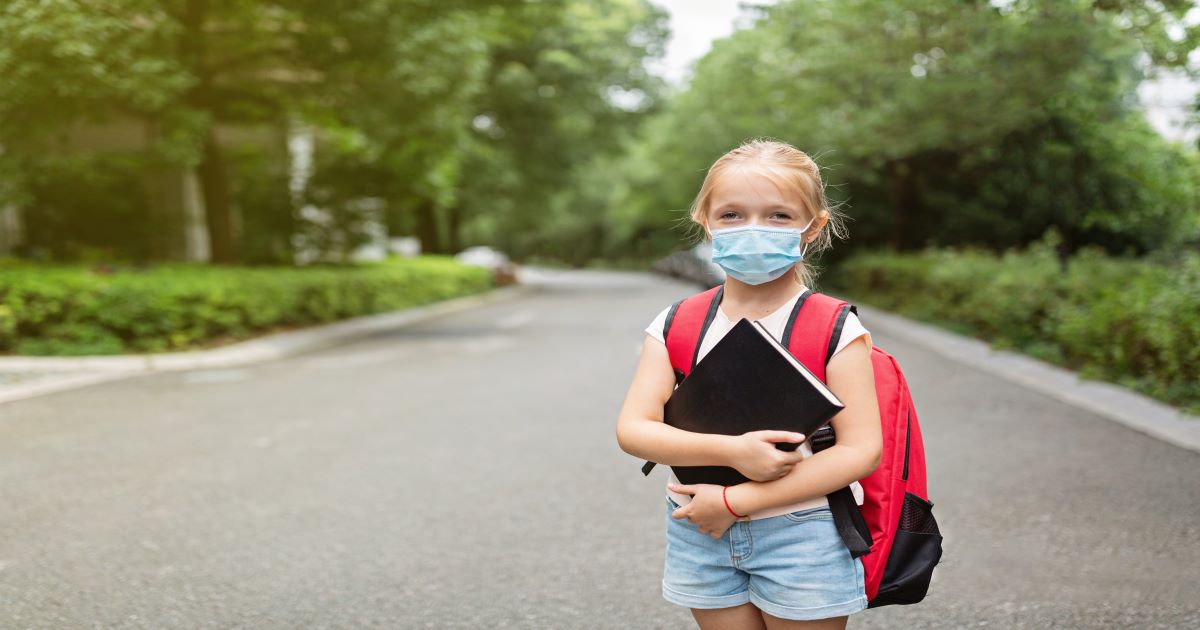 Child waiting for ride to school with mask on